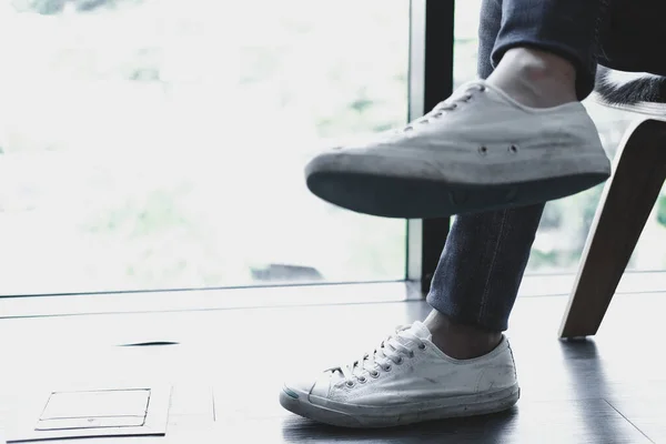 Мужчина подростковые ноги в белых кроссовках сидя расслабляясь в доме — стоковое фото