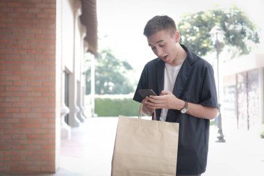 Elinde kağıt poşetler ve cep telefonu olan şaşırmış bir adam. 