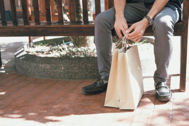 Alışveriş merkezinde elinde poşetlerle dinlenen bir adam.. 