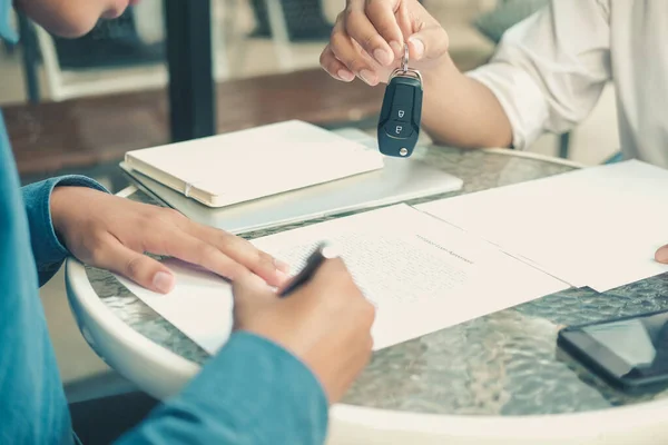 Dealer salesman giving car key to owner. client signing insuranc — Stock Photo, Image