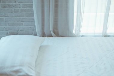 beyaz yastık yatak üzerinde yanında saf pencere perdesinin arkasını görüyor