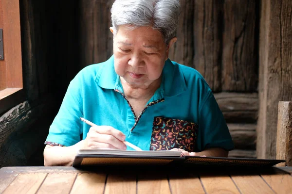 asian elderly female elder woman writing note at home. senior leisure lifestyle