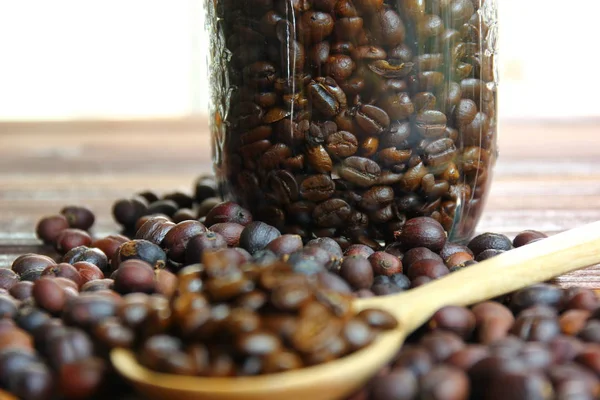 cam şişede kahve çekirdekleri .kavrulmuş kahve çekirdekleri ile kurutulmuş kahve çekirdekleri .kahverengi ahşap zemin üzerinde ahşap kaşık kahve çekirdekleri .