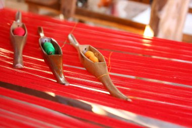 Ahşap mekikte iplik, dokuma tezgahında kırmızı iplikler, soyut arka plan.