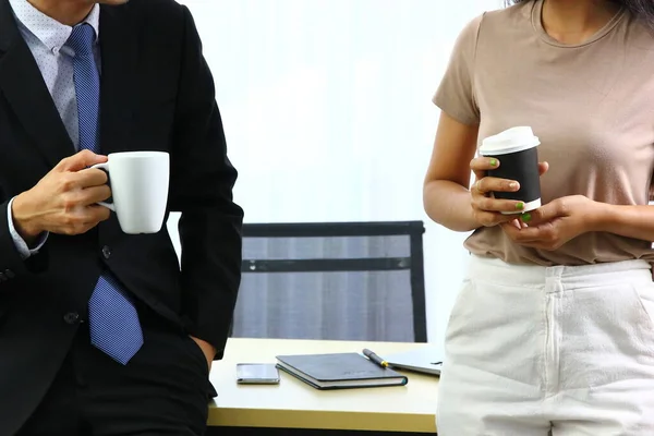 Takım elbiseli bir iş adamı sıcak kahve tutuyor ve kahve molasında Asyalı bir kadınla konuşuyor..