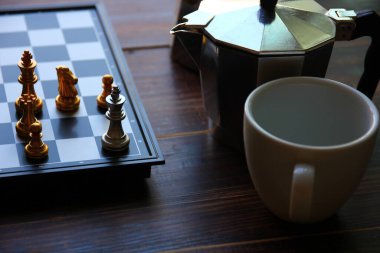 Satranç tahtasının köşesindeki satranç tahtasında boş beyaz seramik kahve fincanıyla satranç oynuyor.