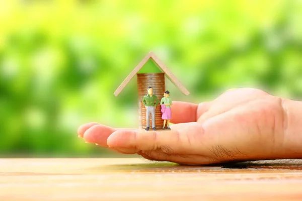 Madeni paraların önünde duran erkek ve kadın figürleri küçük ahşap çatılı, ev kredisi konsepti