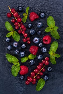 Frenk üzümü, ahududu ve yaban mersini ve nane taze çilek yalan bir siyah arka plan üzerine bırakır. Üstten Görünüm.