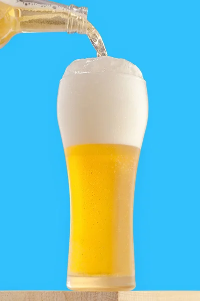 A tall glass with a light chilled beer on a blue background. Beer is poured into a glass.