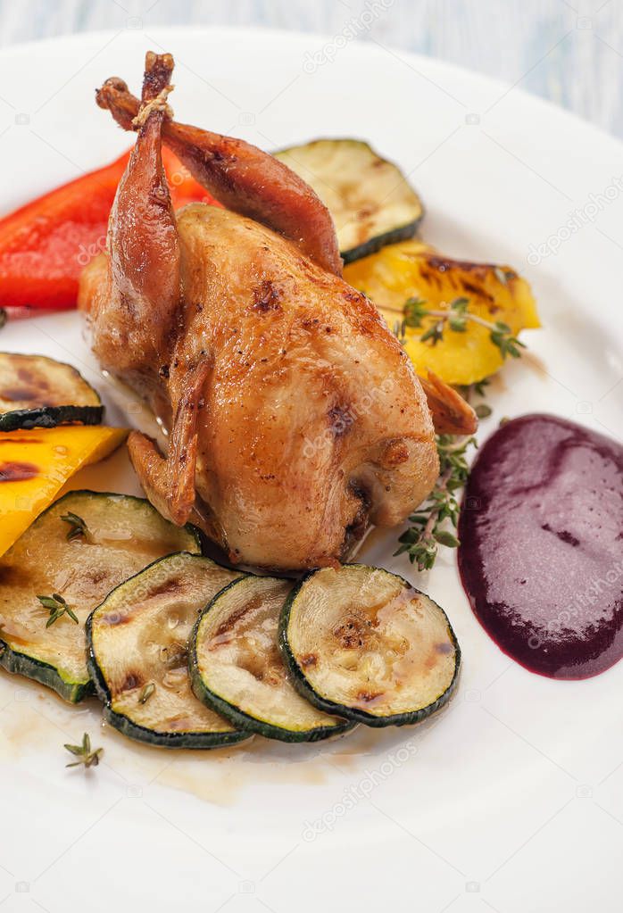 Homemade baked quails with grilled zucchini and pepper garnish and berry sauce. On a white plate. Lunch and dinner for diet. Ketogenic diet. Vertical view.