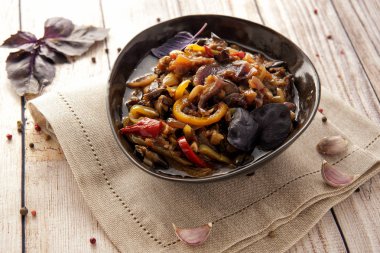 Kalın bir sos içinde haşlanmış aromatik sebzeler. Kafkas mutfağının geleneksel yemeği. Patlıcan, biber ve domates sarımsak ve otlar ile bitkisel yağda. Ketojenik yiyecek. Ahşap bir arka plan ve doğal bir peçete üzerinde bir tabak ta. Yatay görünüm.