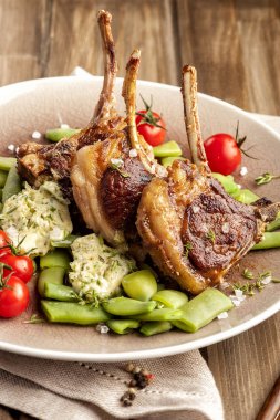 Yeşil fasulye ve kokulu tereyağı bir garnitür ile ızgara kuzu pirzola. Domates ve taze kekik ile. Ev yapımı pişmiş yemek. Ketojenik yiyecek. Tahta bir masa ve doğal bir peçete. Dikey görünümü kapat. 