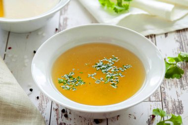 Cooked hot bone broth with spices and fresh herbs. Medical dietary broth and superfood. For ketogenic diet and paleo diet. Serve on an individual plate on a wooden background and with a white napkin. clipart