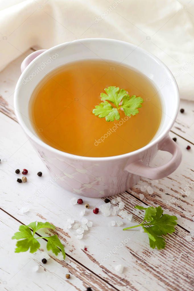 Cooked hot bone broth with spices and fresh herbs. Medical dietary broth and superfood. For ketogenic diet and paleo diet. Serve on an individual plate on a wooden background and with a white napkin.
