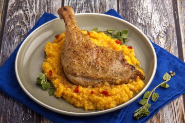 Kabak püresi ve taze otlar ile kavrulmuş ördek bacak. Ahşap bir masada mavi peçete ile bir plaka üzerinde büyük kısmı. Yakın çekim ve yatay görünüm. 