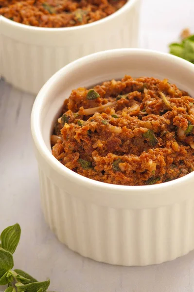 Kırmızı pesto sosu. Kurutulmuş domates, fındık ve taze otlar ile klasik Italyan sosu. Küçük beyaz bir kase hizmet. Yakın çekim ve dikey oryantasyon. 