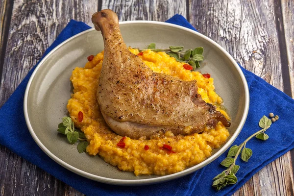 Kabak püresi ve taze otlar ile kavrulmuş ördek bacak. Ahşap bir masada mavi peçete ile bir plaka üzerinde büyük kısmı. Yakın çekim ve yatay görünüm. 