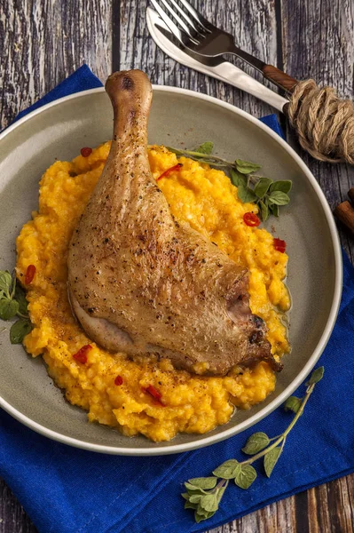 Kabak püresi ve taze otlar ile kavrulmuş ördek bacak. Ahşap bir masada mavi peçete ile bir plaka üzerinde büyük kısmı. Yakın çekim ve dikey görünüm. 