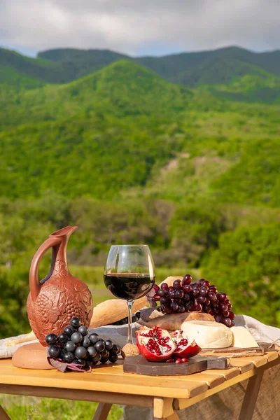 Outdoor picnics in the mountains. A picnic table set with red wine, cheese, fruits, grapes and bread stands in a meadow in green grass. The concept of secluded outdoor recreation.