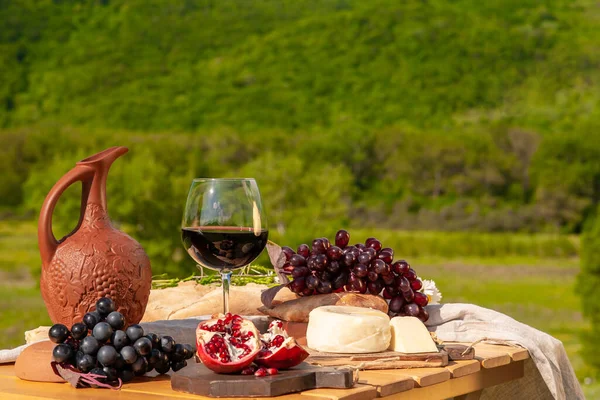 Outdoor picnics in the mountains. A picnic table set with red wine, cheese, fruits, grapes and bread stands in a meadow in green grass. The concept of secluded outdoor recreation.