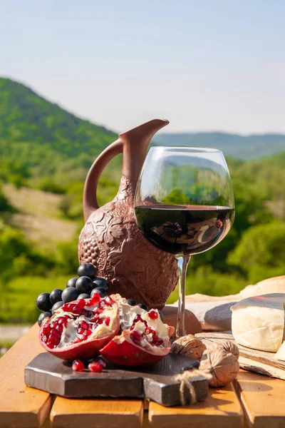 Outdoor picnics in the mountains. A picnic table set with red wine, cheese, fruits, grapes and bread stands in a meadow in green grass. The concept of secluded outdoor recreation.