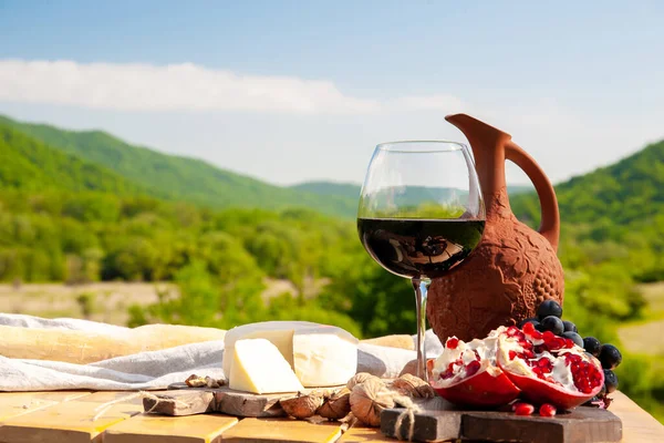 Outdoor picnics in the mountains. A picnic table set with red wine, cheese, fruits, grapes and bread stands in a meadow in green grass. The concept of secluded outdoor recreation.