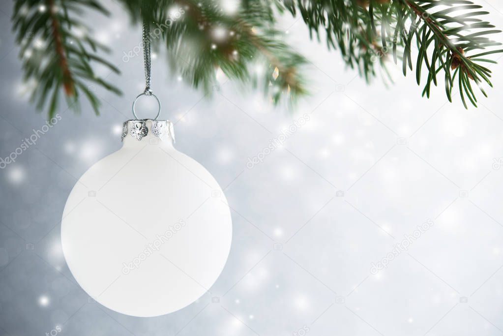 White christmas ball on the xmas tree on silver bokeh background with blurred snow