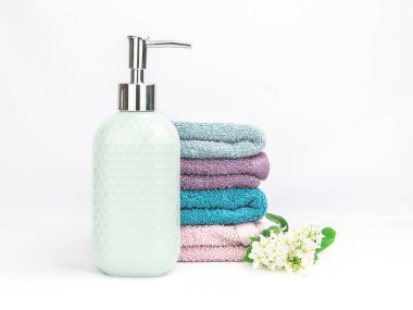 Açık turkuaz seramik sabun makinesi, çok renkli yumuşak havlular ve beyaz arka planda taze çiçekler. Banyo sağlık spa konsepti 