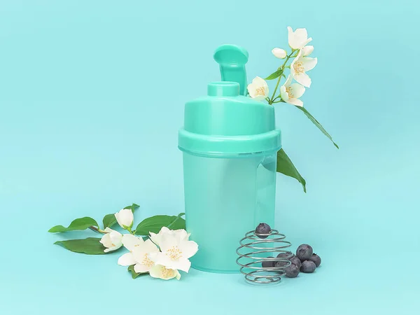 Shaker for sports nutrition with wild berries blueberry and white flowers on cyan background. Healthy lifestyle and diet food concept