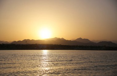 Ufukta dağ siluetleri ile sakin tropik okyanus üzerinde altın günbatımı Manzara görünümü