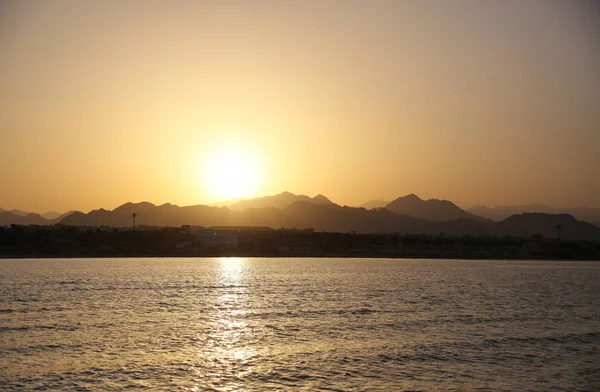 Ufukta dağ siluetleri ile sakin tropik okyanus üzerinde altın günbatımı Manzara görünümü