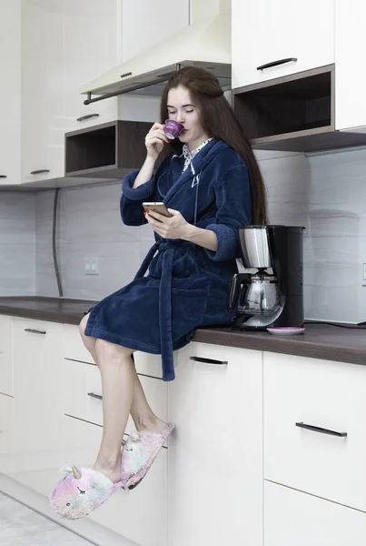 Şık mutfakta sabah kahvesi içen rahat cüppe genç kadın 