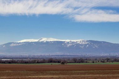 güzel manzara, yeşil çim eniyi ve kahverengi toprak, üstünde kar ile uzun boylu beatiful dağlar, açık mavi gökyüzü ve beyaz bulutlar, Bulgaristan ile geniş alan