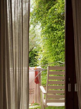 Sardunya 'da çarşaf perdesi ve veranda manzaralı Fransız kapıları ve havlular, eşarplar ve mayo ile kuru raflar.