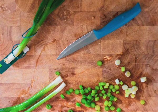 Порезать пружинный лук на деревянной доске рядом с острым синим ножом — стоковое фото