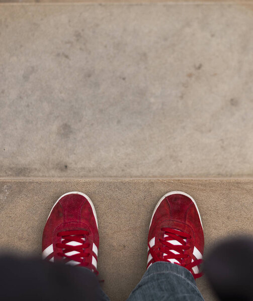 A person stands on the edge of a step wearing bright red trainers.