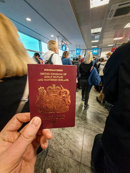 En vit hane innehar sitt röda brittiska pass i handen mitt i en fullsatt avgångs Terminal — Stockfoto