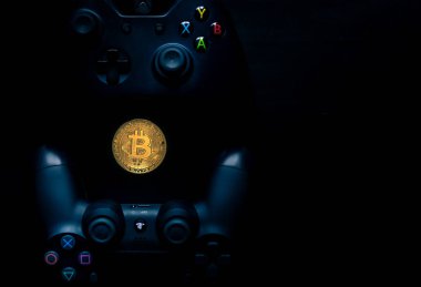 Fiziksel Bir Bitcoin'in yanında Playstation ve Xbox kumandaları.