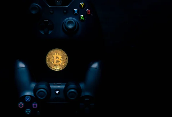 Playstation und Xbox-Controller neben physischem Bitcoin. — Stockfoto