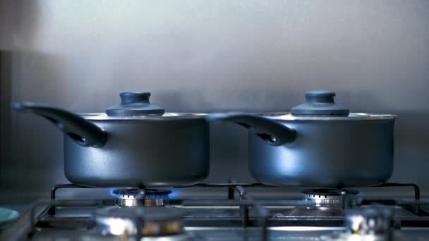 Panelas de cozinha pretas em uma placa de gás emitindo vapor enquanto fervem alimentos no interior — Vídeo de Stock