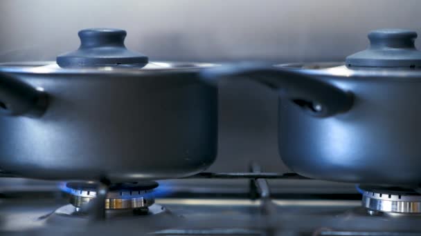Черные кастрюли на газовой плите, излучающей пар, когда они кипятят еду внутри — стоковое видео