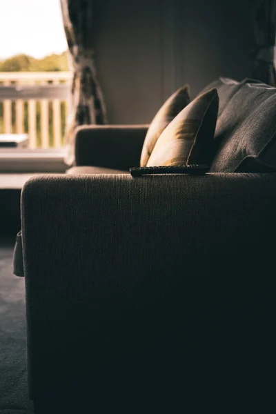 A side on view of a dramatic shot of a two seater sofa with cushions and a remote on the edge