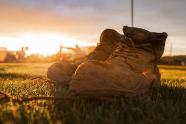 Parlak bir gün batımı önünde çamur kaplı bir şantiyede Güvenlik Boots