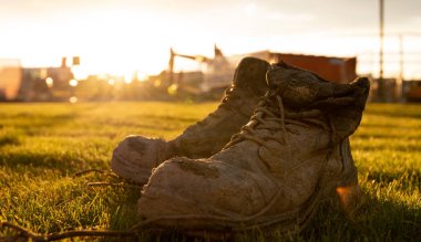 Parlak bir gün batımı önünde çamur kaplı bir şantiyede Güvenlik Boots
