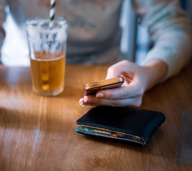 Beyaz bir kadın parlak bir ortamda cep telefonu iken zencefil libir içerken oturdu