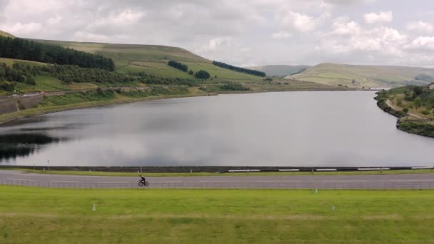 Flygbild över en cyklist som cyklar genom Peak District National Park över en damm mellan Woodhead och Torside, sommar 2019 — Stockvideo