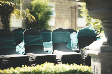 Etraflarında mavi kurdeleli siyah sandalyeler yaz aylarında bir düğünde misafirleri bekliyor dışarıda oturup