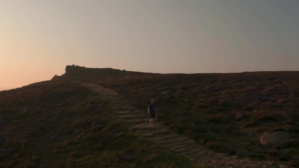 Aerial-na een jonge mannelijke klimmen langs een prachtige heuvel bij zonsondergang — Stockvideo