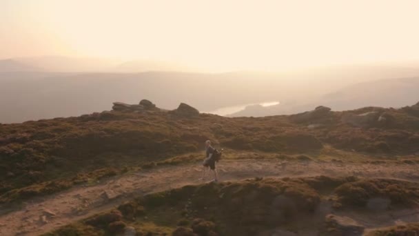 空中 - 夕暮れ時に見事な丘の中腹に沿って登る若い男性に続いて — ストック動画