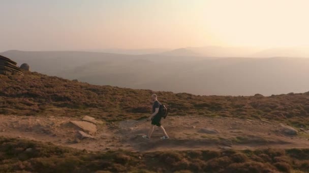 空中 - 跟随一个年轻的男性在日落时沿着令人惊叹的山坡攀登 — 图库视频影像